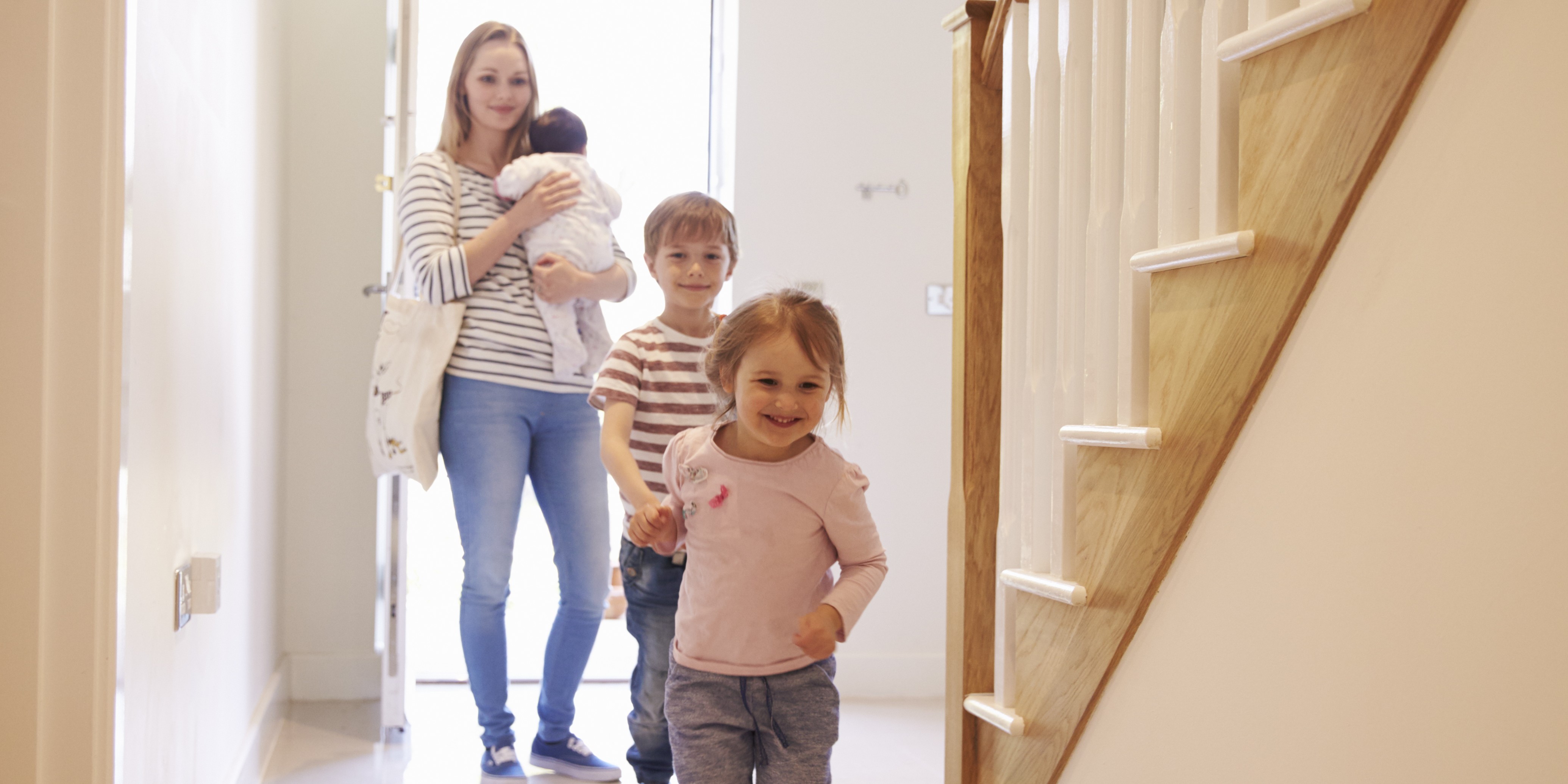 Mor holder baby på armen mens to eldre barn, en gutt og en jente, løper inn i et ubebodd hus.