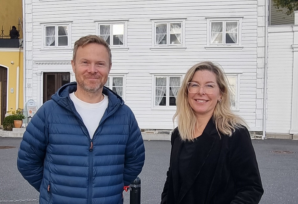 Vidar Åsheim i blå dunjakke og Anette Flaath i sort kåpe står foran Lassens hus. Foto.