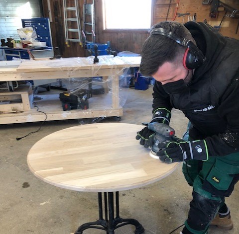 En beboer i arbeid pusser en rund bordplate. Foto.