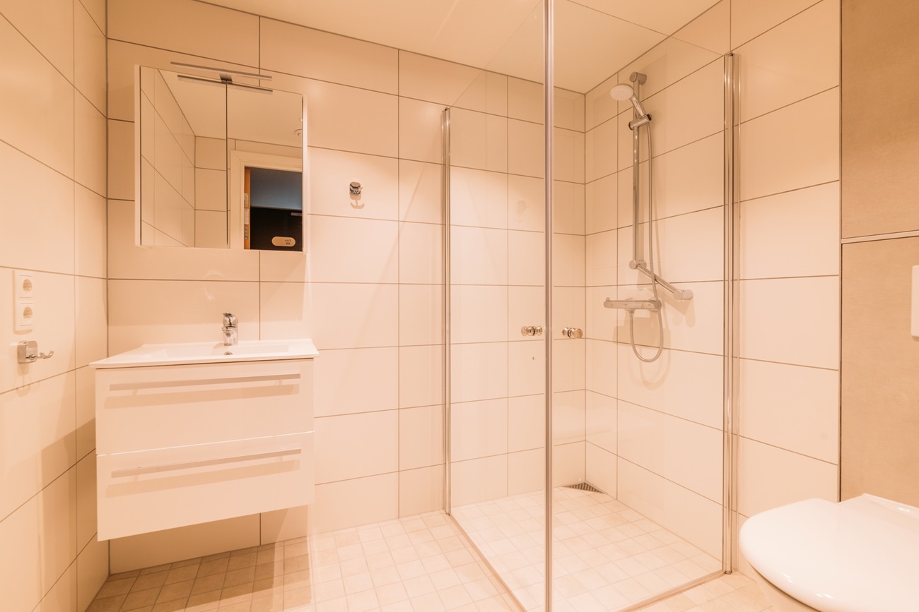 Baderom med hvit innredning og dusjvegger i glass. Foto.