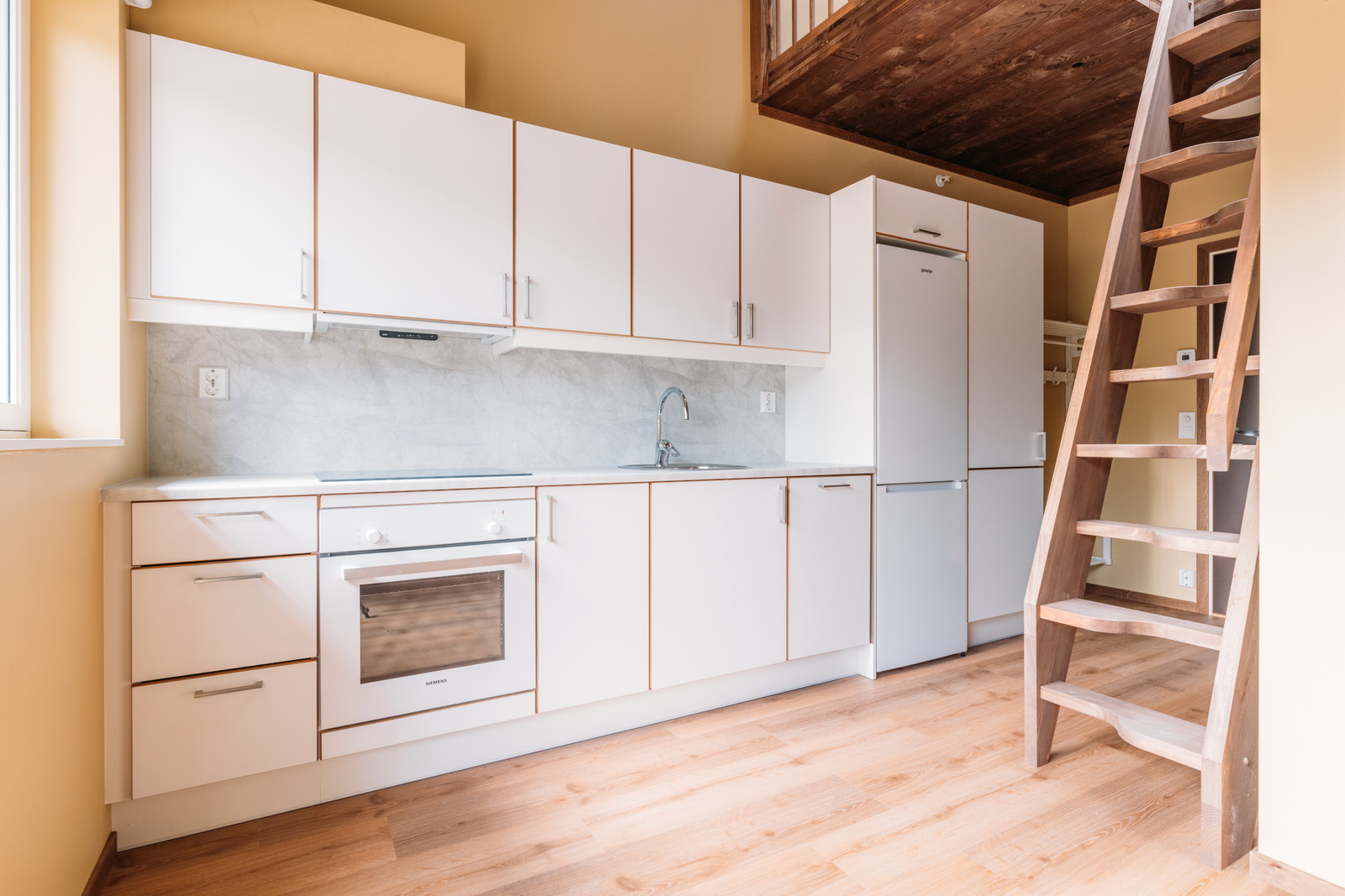 Hvit kJøkkeninnredning med trapp til hems i hybel. Foto.
