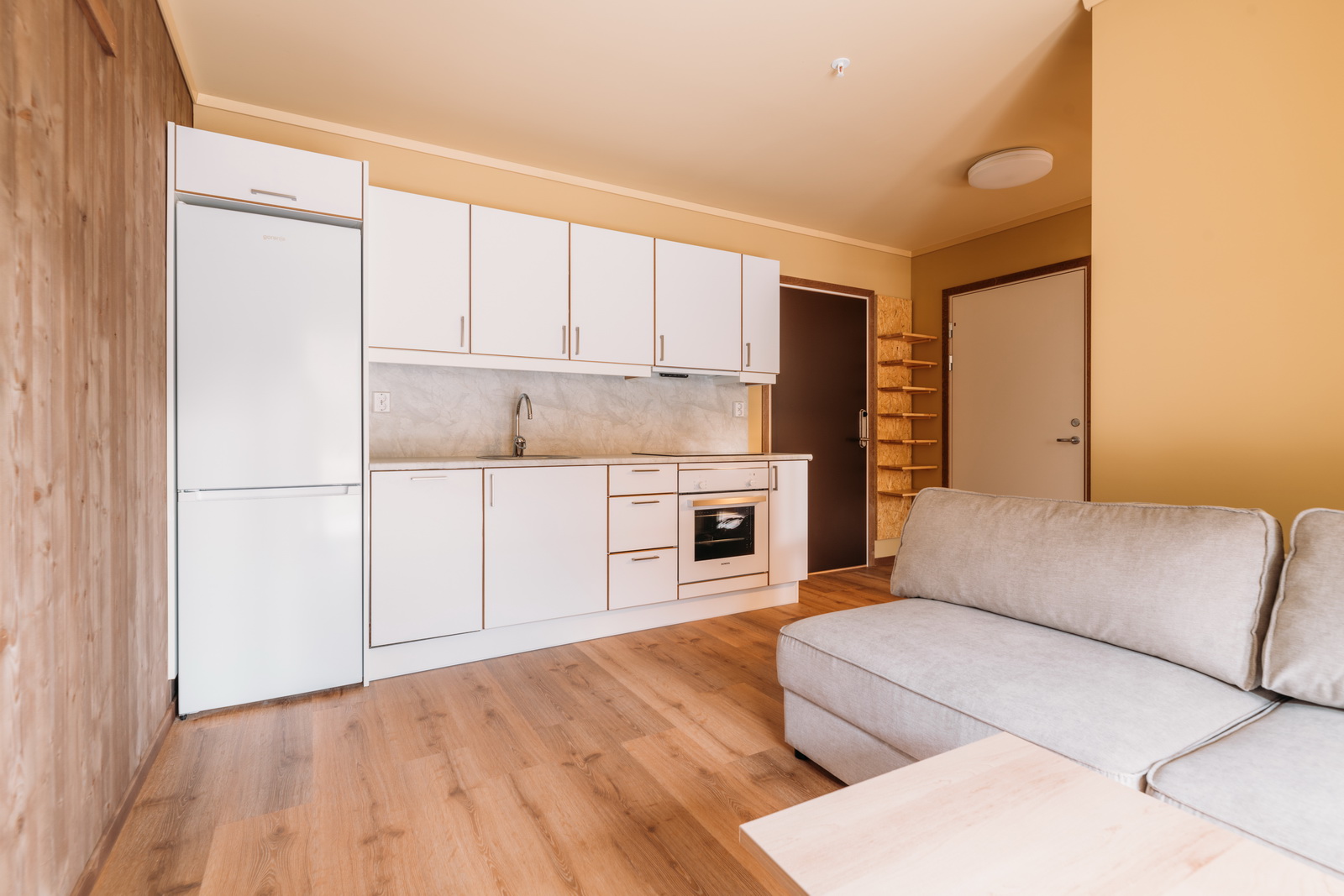 Hvitt kjøkken og stue med sofa i parleilighet. Foto.