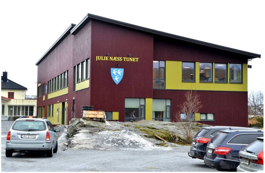 Fasadebilde av det rødmalte bygget med gule vindusrammer og pulttak. Foto.