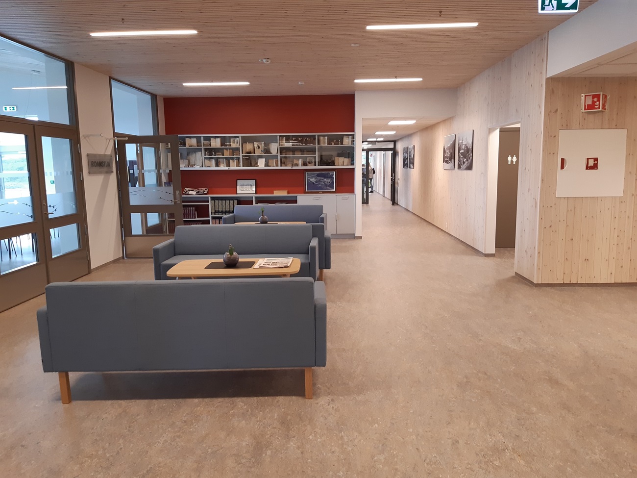 Sosial sone med blå sofaer, lyse trevegger og rød kontrastvegg . Foto.