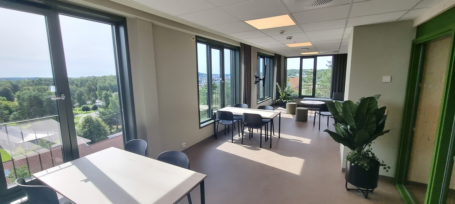 Stort og lyst fellesrom i hver etasje. Store vindusflater med utsikt mot UiA og sentrum. Bord og stoler. Foto. 