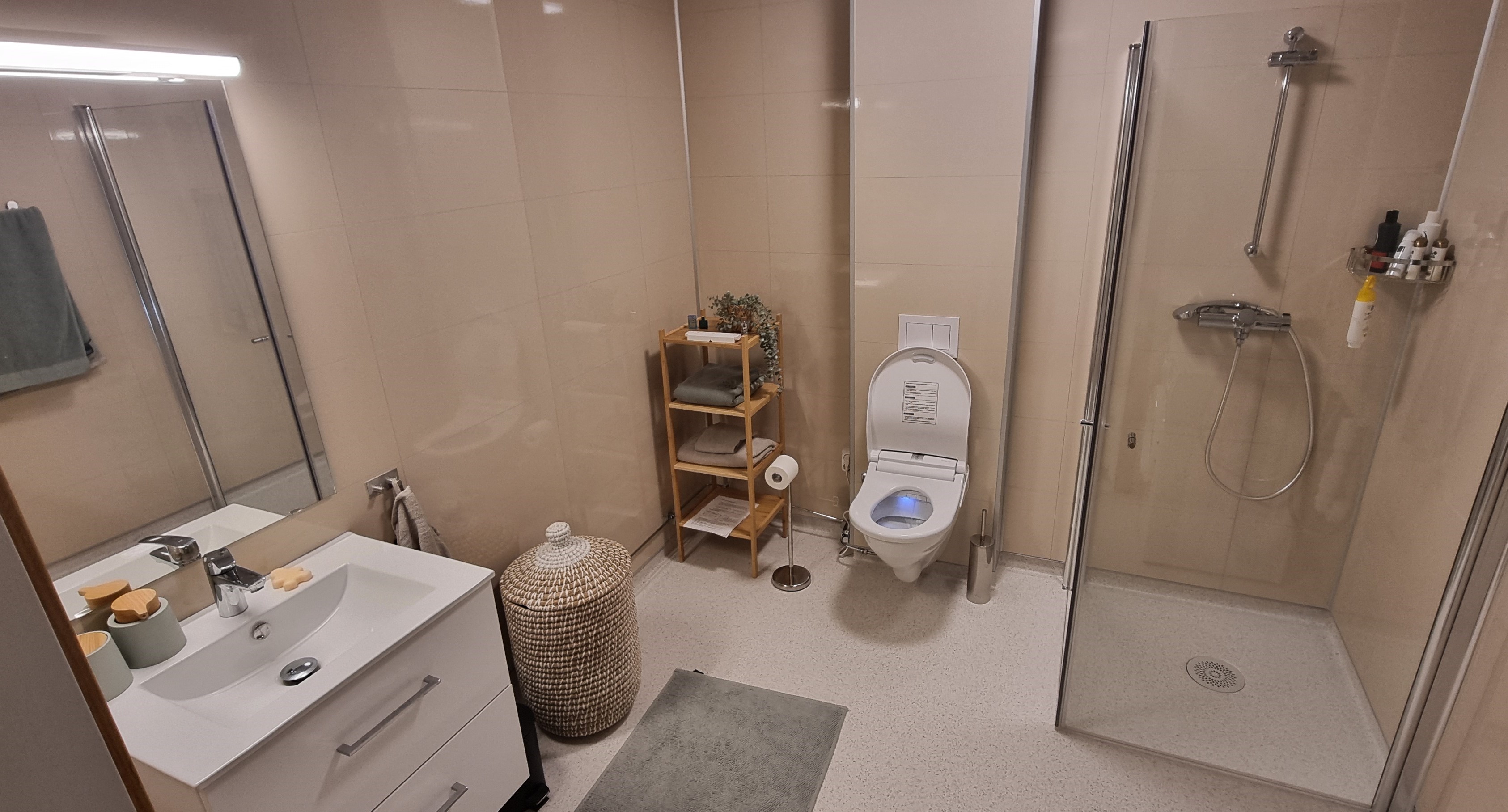 Romslig bad med lyse vegger og hvit innredning og dusjhjørne. Foto. 