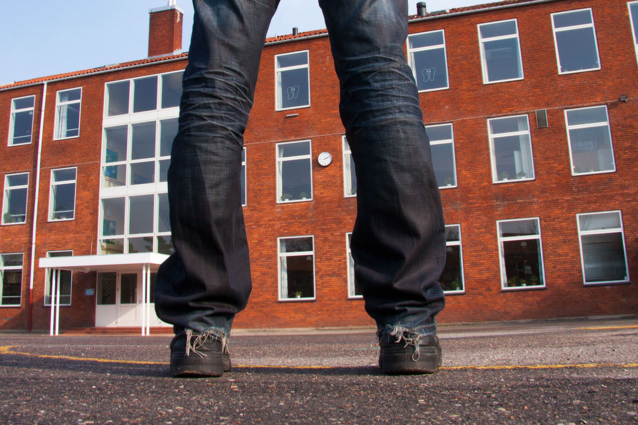 En person står på asfalten foran et offentlig bygg. Foto.