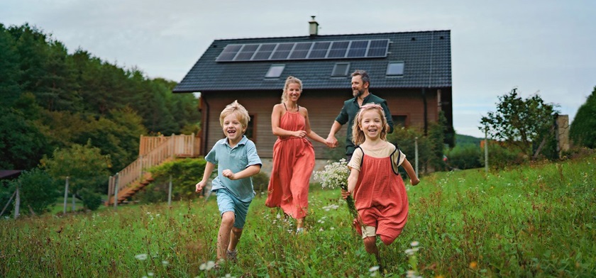 En familie løper i en eng foran et bolighus