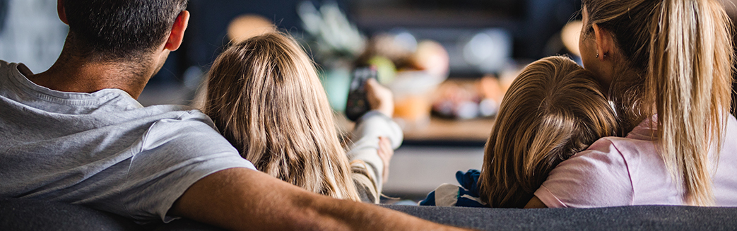familie sett bakfra, sitter sammen i en sofa og ser på tv