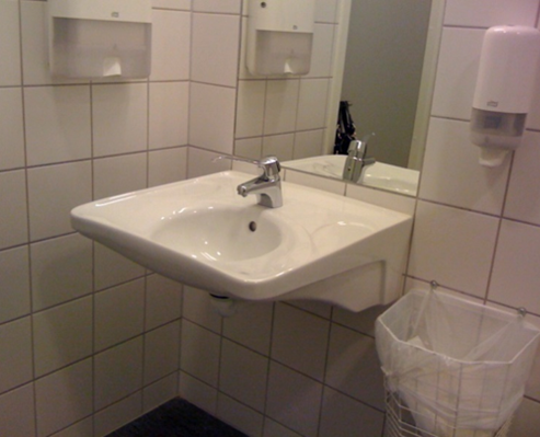Foto av dyp, hvit servant. Speil over og vegghengt søppelkasse ved siden av.