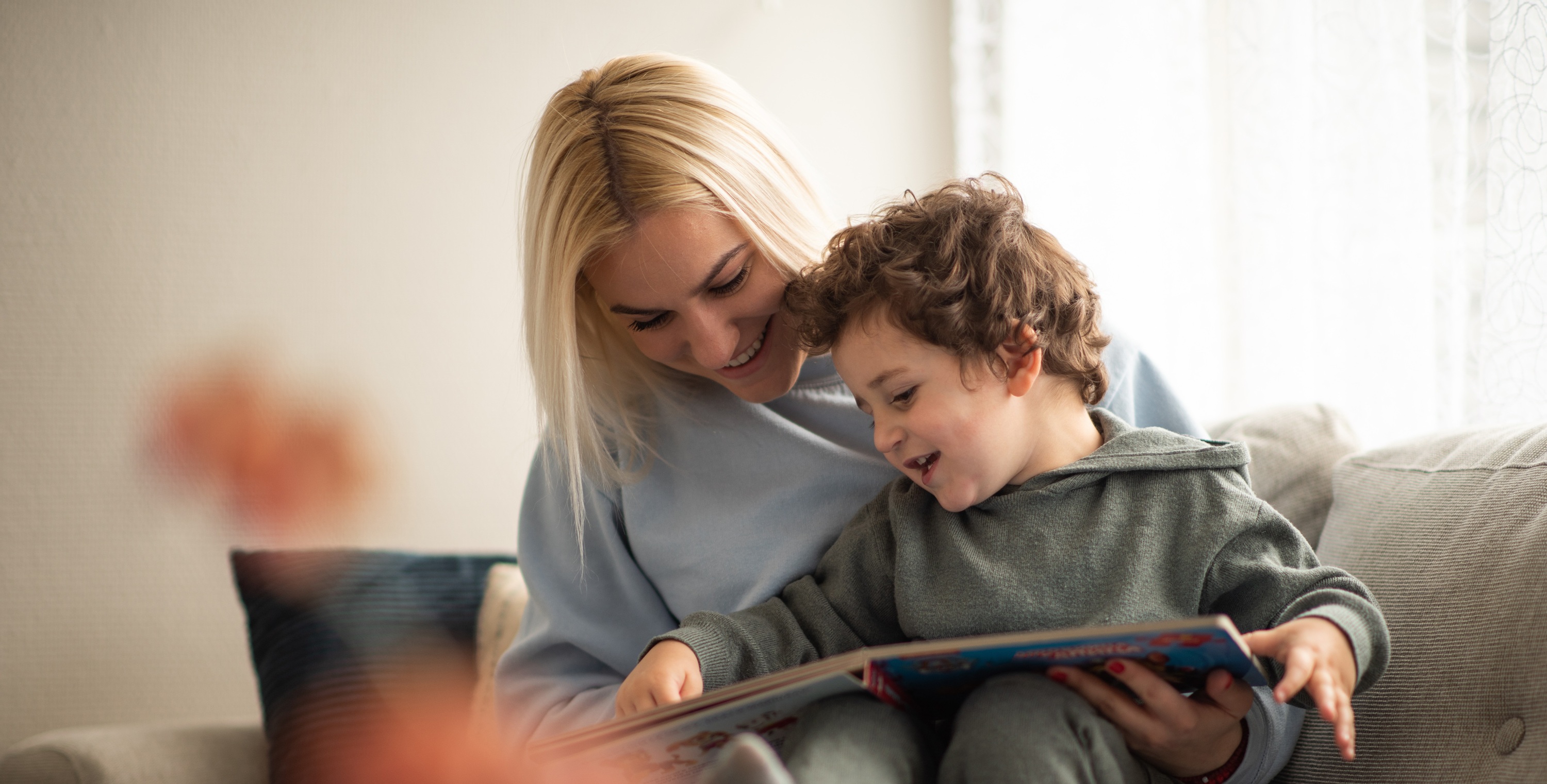 Mor og sønn som leser bok sammen i sofaen. Lys og trivelig stemning. Foto. 