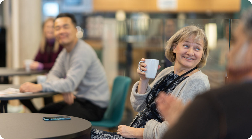 En dame smiler og holder en kaffekopp. Foto.